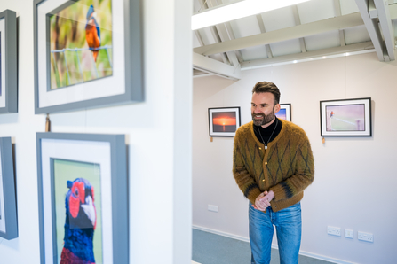 A man smiling and looking at photos at a photography exhibit.