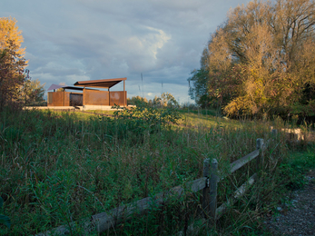 A bird hide structure made of wood and metal, set amongst marshland