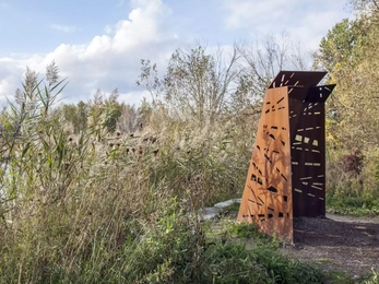 A bird hide structure made of wood with holes cut into it