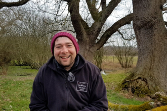 A photo of Matt Wickens at Sweet Briar Marshes. He is wearing an NWT fleece and a wooly hat. 