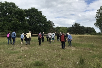 A group of people on a walk through a field on a cloudy day. The people are pictured from behind and are wearing coats.