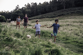 2 adults and 2 children enjoying themselves walking out in nature. The children are running down a small hill while the adults hold hands.