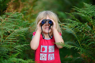 A young girl smiles as she looks though a pair of binoculars