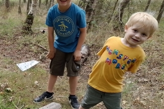 Two young boys stand in a wood and smile happily at the camera