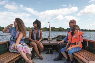 Four people wearing life vests, smiling whilst out on the broads on one of our boat trips