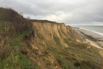Sandy, grassy cliffs sweep down to a beach on a grey day