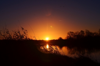 A bright orangey yellow sunrise appears over a river