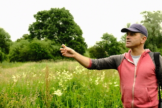 Our ambassador Nick Acheson is holding a piece of grass as he hosts a wildflower walk at Sweet Briar Marshes