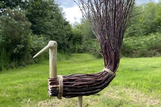 Brush-tailed bird statue, with its body and tail made from sticks that are tied in bundles
