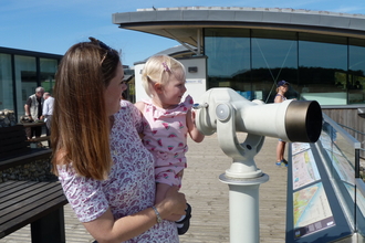 A mum and daughter looking through a telescope at Cley visitor centre