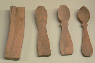 Six pieces of wood next to each other progressively carved starting with a small branch covered in bark to a completed carved spoon on the right