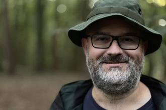 A close up of Iain Robinson, he has a grey beard, black glasses and a khaki hat on.