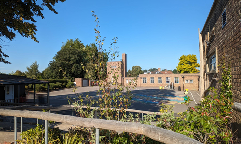 A school playground surrounded by brick buildings and plants, under a clear blue sky