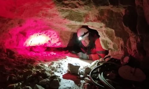 Ecologist wearing a helmet with a light on it crawling into a cave