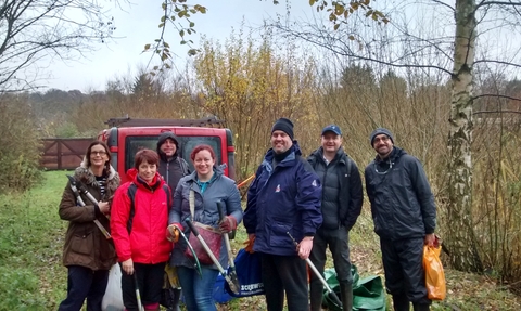 A group of people wearing winter clothes smile at the camera as they hold litter pickers