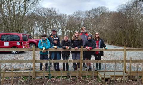 A group of young people stand behind a fence smiling on a cloudy day