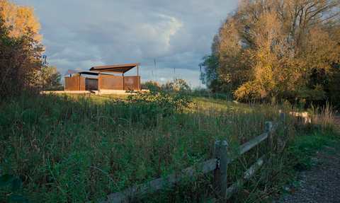 A bird hide structure made of wood and metal, set amongst marshland