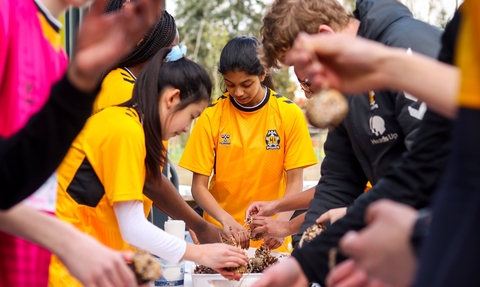 Young people wearing football shirts gathered around a table making bird feeders