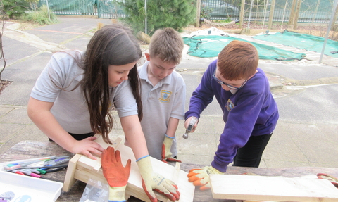 Three children use tools to build a nestbox in a playground