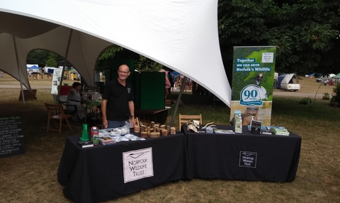 A man wearing an NWT t-shirt stands behind a stall covered with items, underneath a white tent in a field