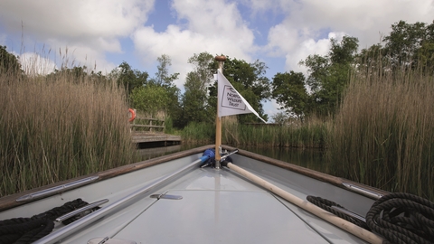 A boat with a NWT flag sailing through reeds.