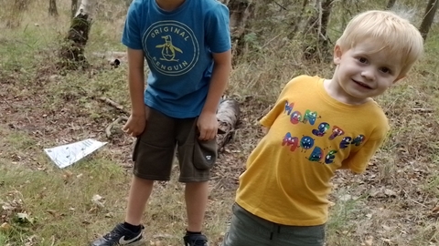 Two young boys stand in a wood and smile happily at the camera