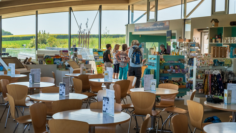 NWT Cley Visitor Centre, showing tables and chairs, welcome desk and views through large glass walls onto the nature reserve
