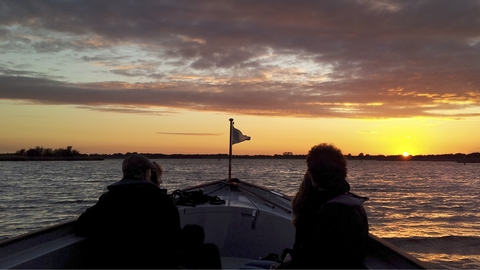 Passengers looking out from a boat at dawn at Hickling Broad