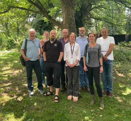 A group of campaigners standing in front of a tree on a sunny day. There are eight people, all looking at the camera and dressed in casual clothing