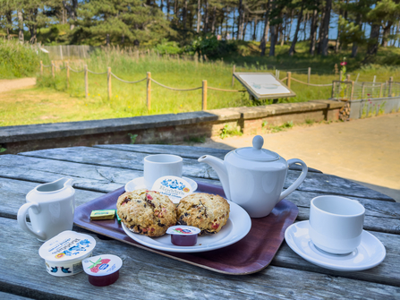 A cream tea on a wooden table outside at Holme visitor centre