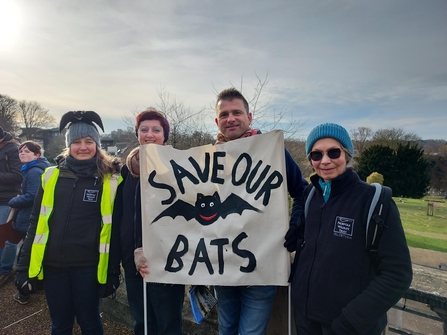A group of people are protesting a new road. They are holding a sign which reads save our bats