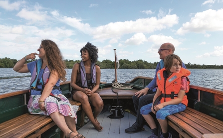 Four people wearing life vests, smiling whilst out on the broads on one of our boat trips