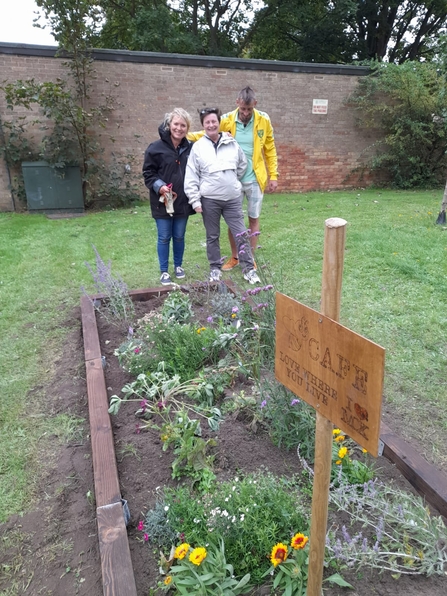 Three people stand by a finished sleeper border of flowers while they smile at the camera