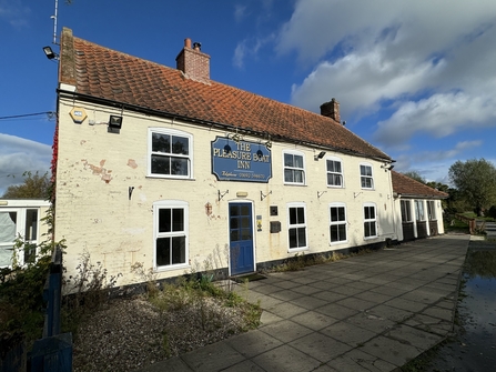 The Pleasure Boat Inn pub under a blue sky. The building is painted white, with a blue sign above a blue door