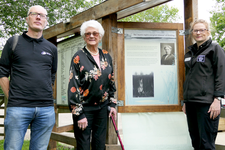 Three people stand by a newly unveiled panel depicting the life and work of naturalist Emma Turner