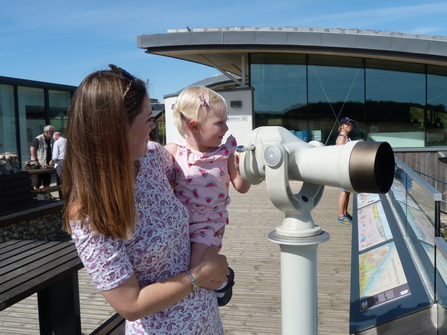 A mum and daughter looking through a telescope at Cley visitor centre