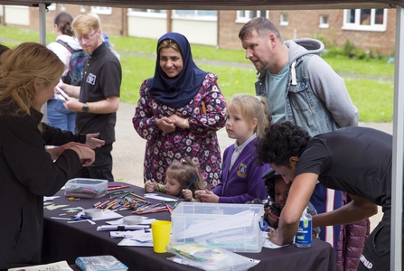 Families chatting to NWT staff at a stall on Lefroy Estate. Some children and making use of the colouring pencils and paper on the stall. 