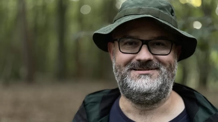 A close up ofIan Robinson, he has a grey beard, black glasses and a khaki hat on. 