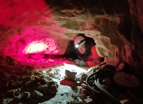 Ecologist wearing a helmet with a light on it crawling into a cave