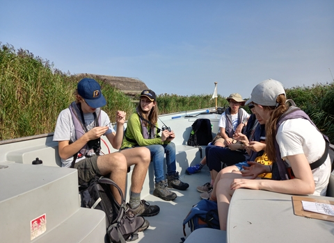 A group of young people sit in a boat on a sunny day