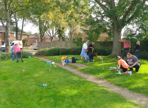 A group of people plant bulbs in patches of grass on a sunny day