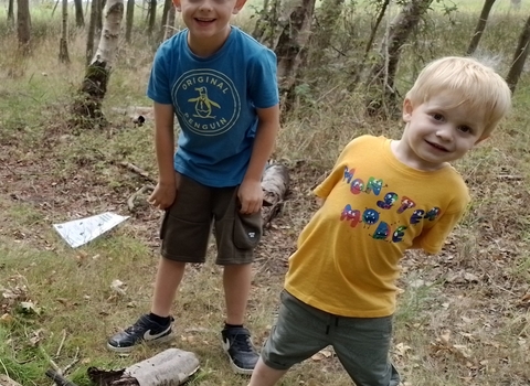 Two young boys stand in a wood and smile happily at the camera