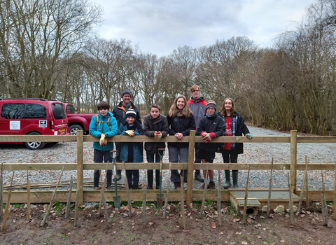 A group of young people stand behind a fence smiling on a cloudy day