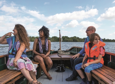 Four people wearing life vests, smiling whilst out on the broads on one of our boat trips