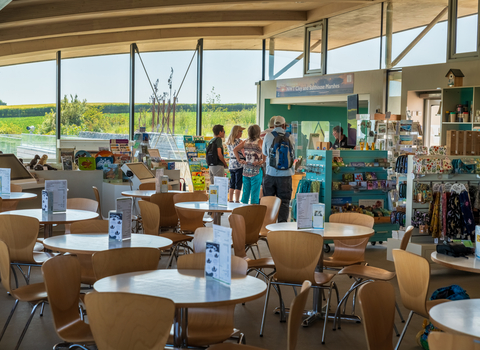 NWT Cley Visitor Centre, showing tables and chairs, welcome desk and views through large glass walls onto the nature reserve