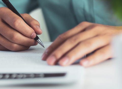 A person writing a letter, with their hands in close up as they hold a pen in their right hand