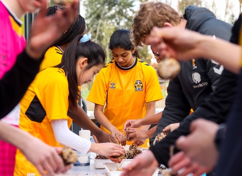 Young people wearing football shirts gathered around a table making bird feeders