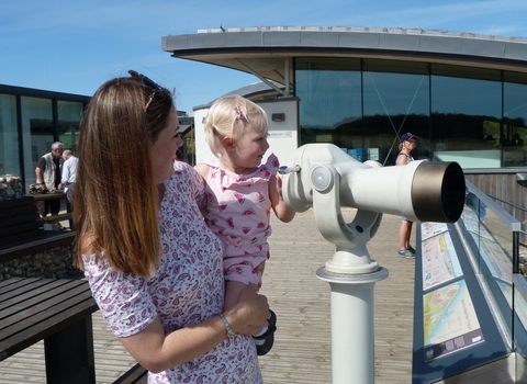 A mum and daughter looking through a telescope at Cley visitor centre