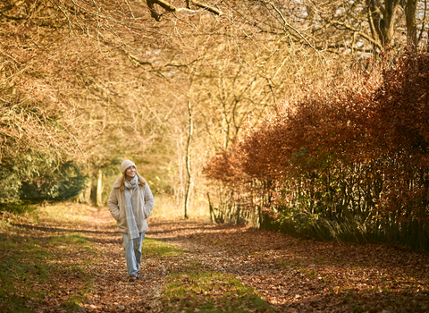 A woman walks down a path strewn with fallen leaves in the autumn