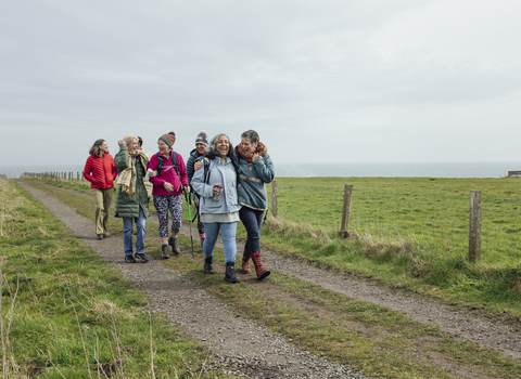 Dressed in winter clothes, a group of people walk along a track smiling and laughing